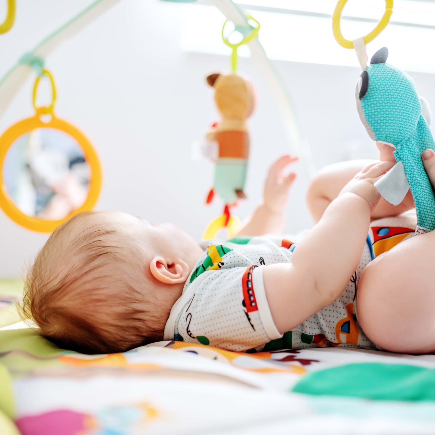 Adorable six months old boy lying in bed and playing with crib toys. Healthy upbringing concept.